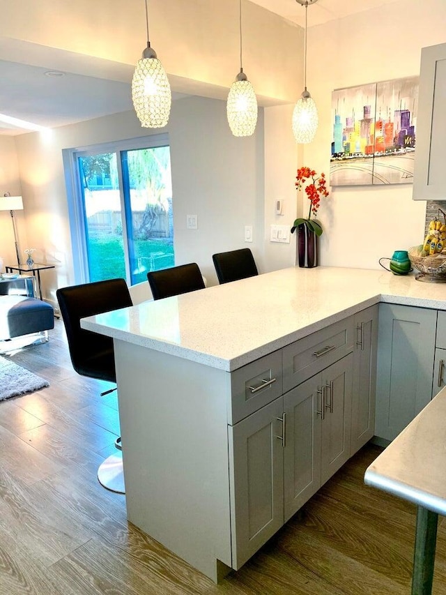 kitchen with pendant lighting, gray cabinetry, a kitchen bar, dark hardwood / wood-style flooring, and kitchen peninsula