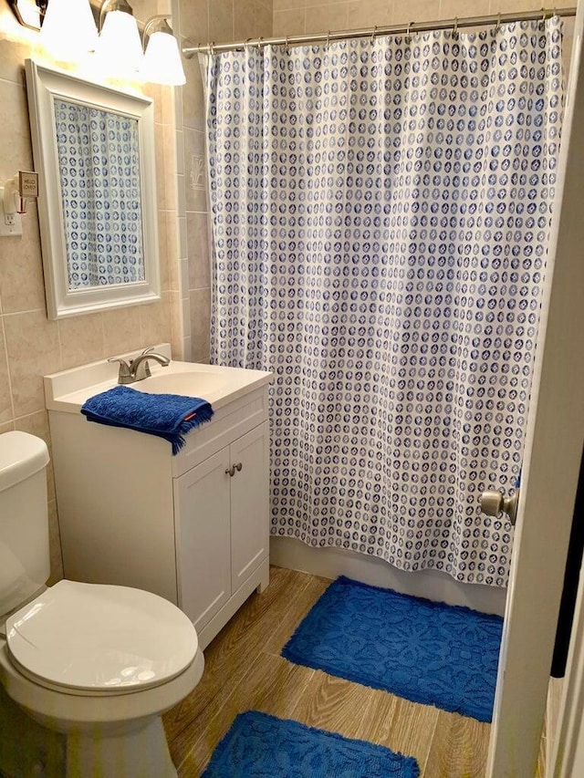 bathroom featuring hardwood / wood-style floors, tile walls, vanity, walk in shower, and toilet