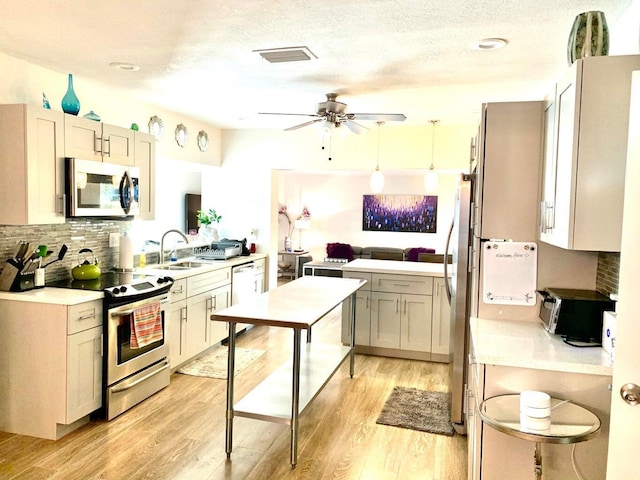 kitchen with sink, tasteful backsplash, pendant lighting, stainless steel appliances, and light hardwood / wood-style floors