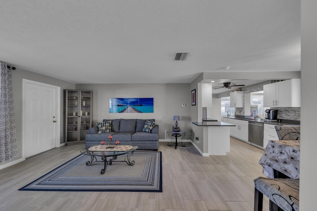 living room featuring ceiling fan, light hardwood / wood-style floors, and a textured ceiling