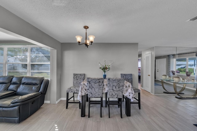 dining area with light hardwood / wood-style floors, a textured ceiling, and a notable chandelier