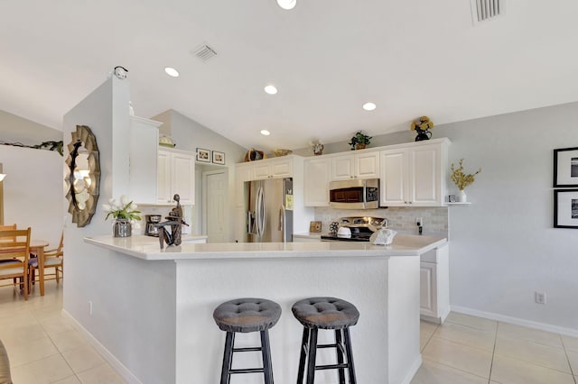 kitchen with light tile patterned flooring, vaulted ceiling, kitchen peninsula, stainless steel appliances, and white cabinets