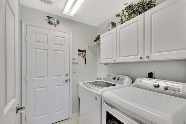 laundry room featuring cabinets, light tile patterned floors, and washing machine and clothes dryer