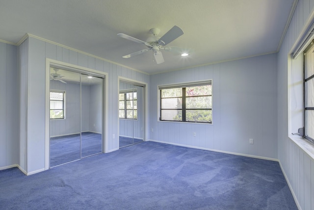 unfurnished bedroom featuring dark colored carpet, ceiling fan, ornamental molding, and two closets