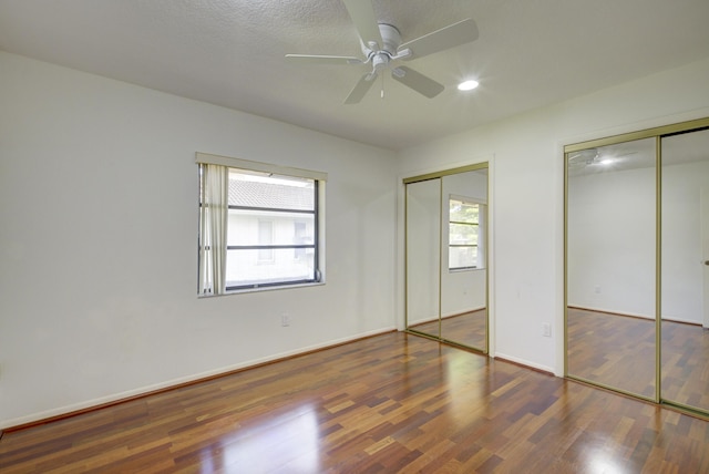 unfurnished bedroom featuring dark wood-type flooring, ceiling fan, and two closets