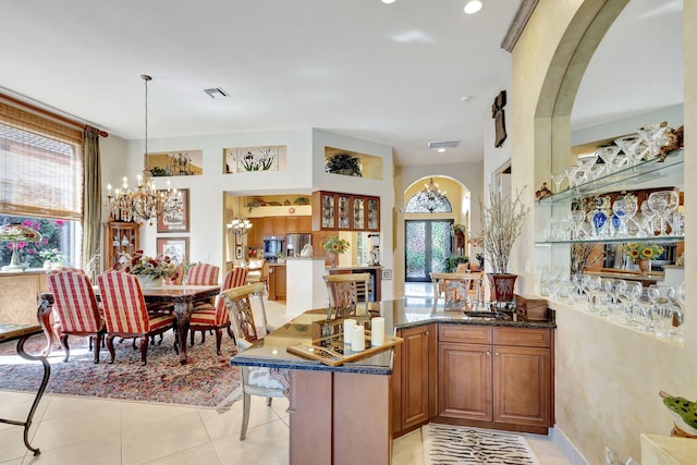 kitchen featuring light tile patterned flooring, a breakfast bar, an inviting chandelier, decorative light fixtures, and dark stone counters