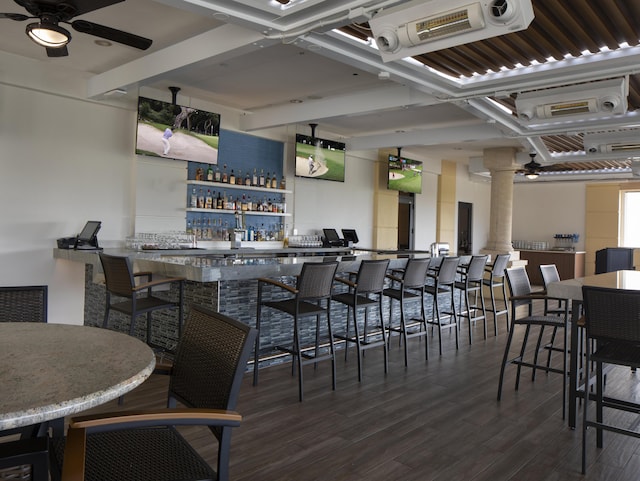 interior space with ceiling fan, bar, dark hardwood / wood-style flooring, and ornate columns