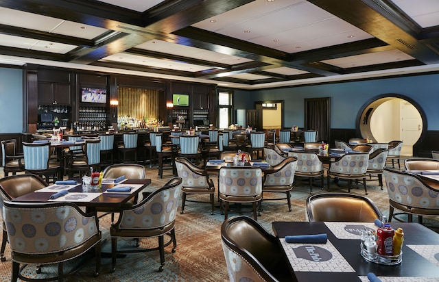 dining space featuring crown molding, bar area, coffered ceiling, and beam ceiling