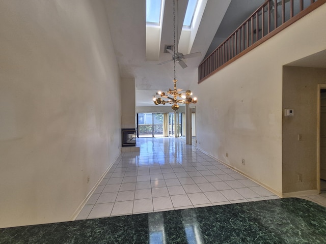 tiled empty room featuring a high ceiling, a chandelier, and a skylight