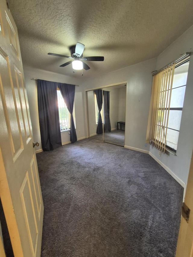 empty room featuring ceiling fan, a textured ceiling, and dark colored carpet