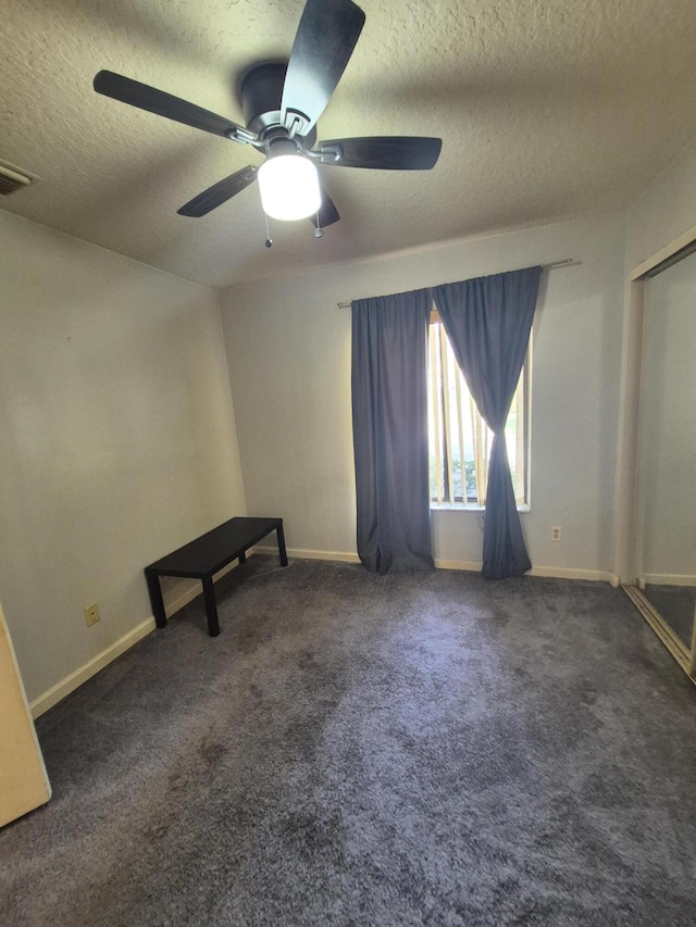 unfurnished room with ceiling fan, a textured ceiling, and dark colored carpet