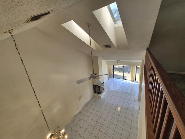 corridor featuring lofted ceiling with skylight, a textured ceiling, and light tile patterned flooring