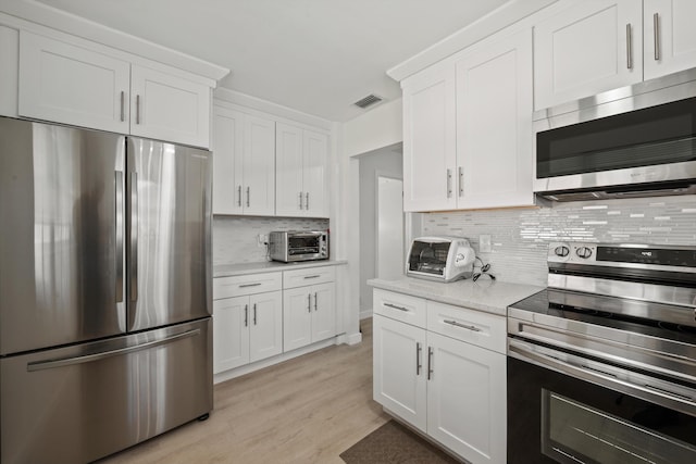 kitchen featuring white cabinetry, light stone counters, light hardwood / wood-style flooring, stainless steel appliances, and decorative backsplash