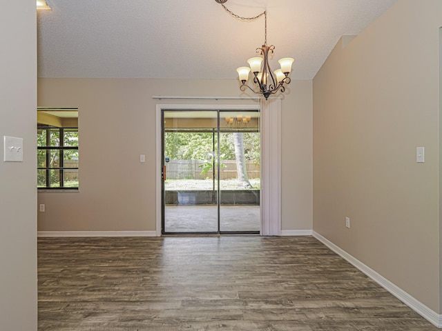 spare room with a healthy amount of sunlight, a chandelier, and dark hardwood / wood-style floors