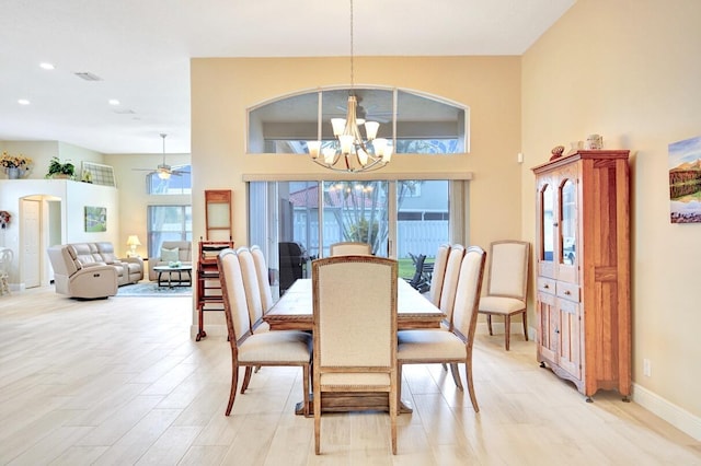 dining room with ceiling fan with notable chandelier, light hardwood / wood-style flooring, and a high ceiling