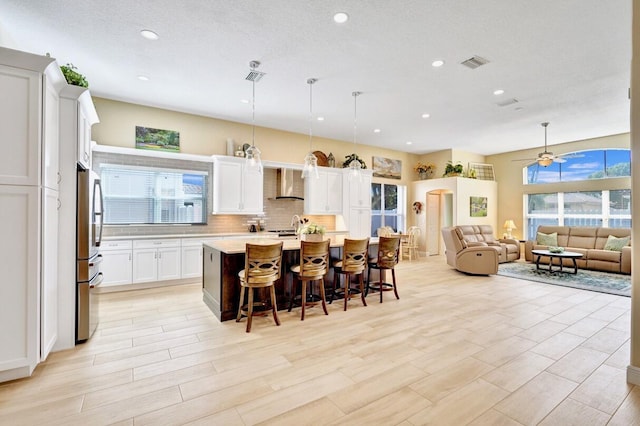 kitchen featuring a breakfast bar, stainless steel refrigerator, decorative light fixtures, white cabinetry, and a center island with sink