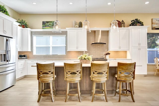 kitchen with a kitchen island, wall chimney exhaust hood, stainless steel fridge, and hanging light fixtures