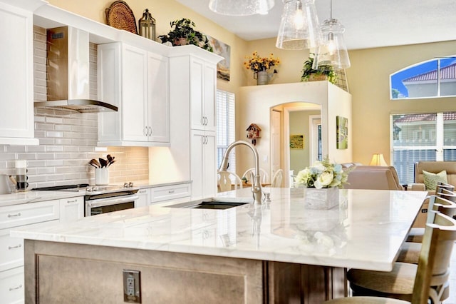 kitchen with stainless steel range, wall chimney exhaust hood, a center island with sink, and white cabinets