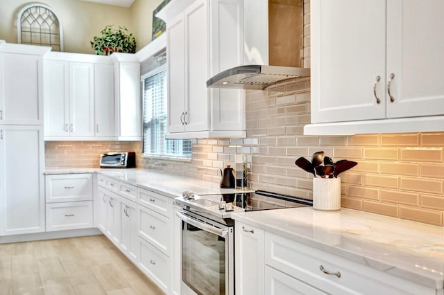 kitchen with backsplash, light stone counters, white cabinets, stainless steel electric range oven, and wall chimney exhaust hood