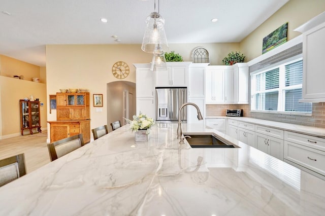 kitchen featuring white cabinetry, sink, stainless steel fridge, and hanging light fixtures