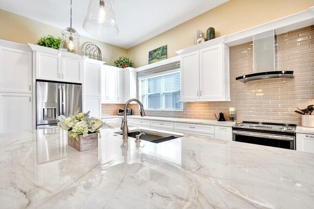 kitchen with wall chimney exhaust hood, sink, white cabinetry, decorative light fixtures, and stainless steel appliances