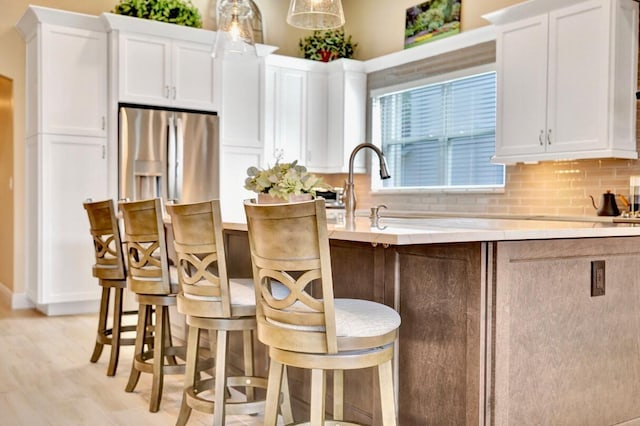 kitchen featuring white cabinetry, a kitchen bar, hanging light fixtures, and tasteful backsplash