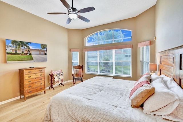 bedroom featuring ceiling fan, wood-type flooring, a fireplace, and a towering ceiling