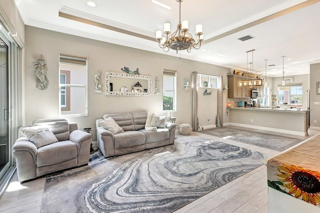 living room featuring a chandelier, ornamental molding, a raised ceiling, and light hardwood / wood-style floors