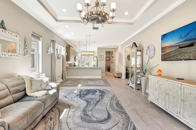 living room with crown molding, light hardwood / wood-style flooring, a notable chandelier, and a tray ceiling