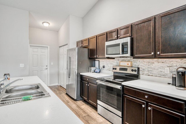 kitchen featuring sink, appliances with stainless steel finishes, dark brown cabinets, tasteful backsplash, and light hardwood / wood-style floors