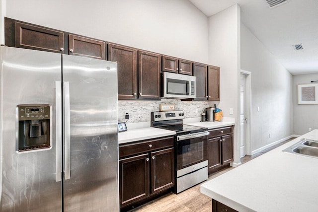 kitchen featuring appliances with stainless steel finishes, tasteful backsplash, lofted ceiling, dark brown cabinetry, and light wood-type flooring