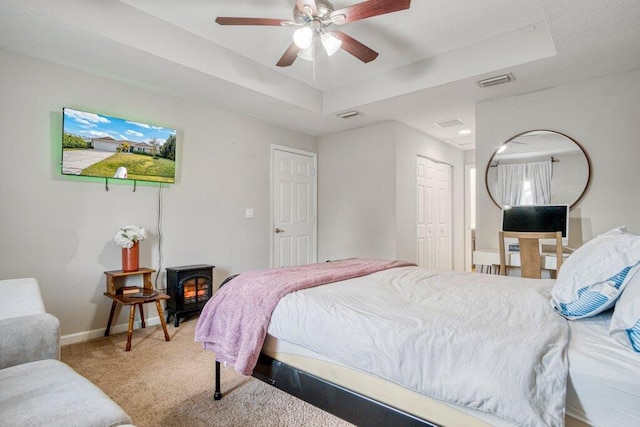 carpeted bedroom featuring ceiling fan, a raised ceiling, a closet, and a wood stove