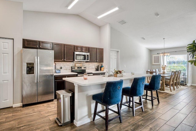 kitchen featuring dark wood-type flooring, hanging light fixtures, a center island with sink, stainless steel appliances, and a kitchen bar