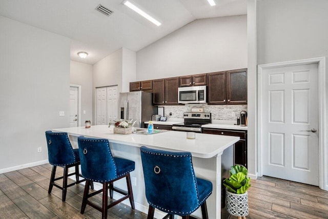 kitchen featuring wood-type flooring, a breakfast bar, an island with sink, and appliances with stainless steel finishes