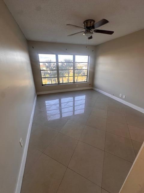 spare room with tile patterned flooring, ceiling fan, and a textured ceiling