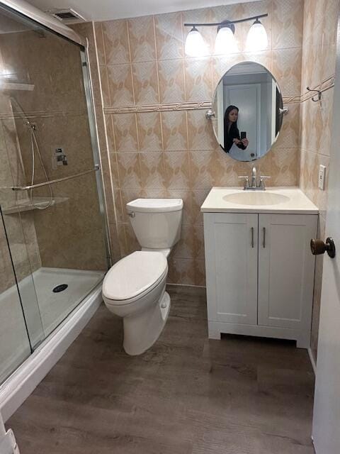 bathroom with hardwood / wood-style flooring, tile walls, vanity, an enclosed shower, and toilet