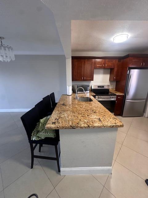 kitchen featuring light tile patterned flooring, sink, appliances with stainless steel finishes, kitchen peninsula, and light stone countertops