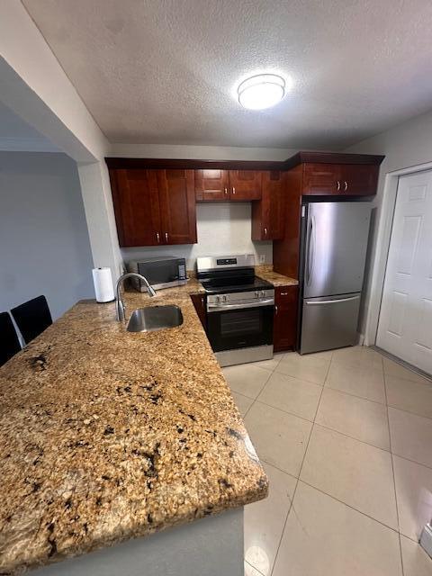 kitchen with sink, light tile patterned floors, stainless steel appliances, light stone countertops, and a textured ceiling