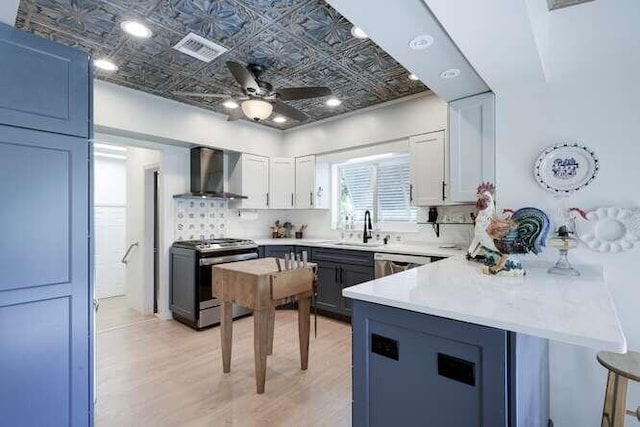 kitchen with white cabinetry, kitchen peninsula, wall chimney range hood, stainless steel range oven, and light hardwood / wood-style flooring