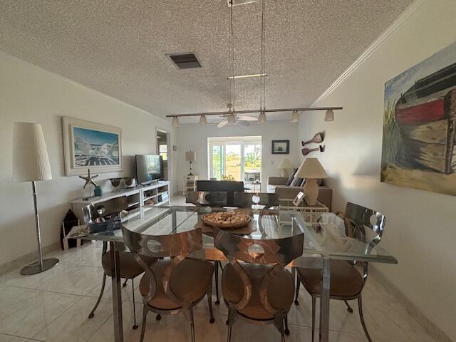 tiled dining room featuring rail lighting, crown molding, ceiling fan, and a textured ceiling