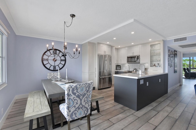 kitchen featuring pendant lighting, an island with sink, white cabinets, light hardwood / wood-style floors, and stainless steel appliances