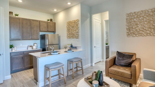 kitchen with sink, light hardwood / wood-style flooring, stainless steel fridge, a breakfast bar area, and kitchen peninsula