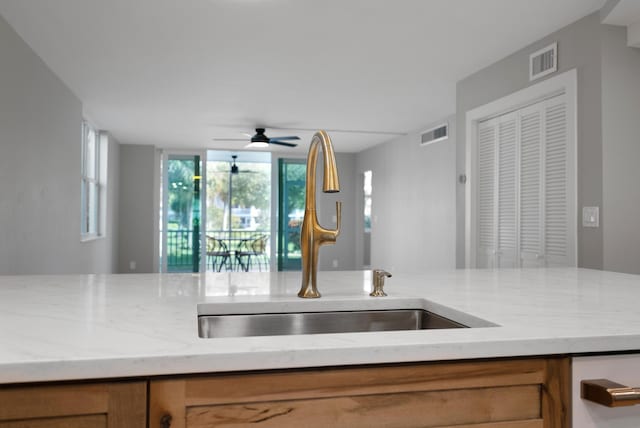 kitchen featuring ceiling fan, light stone countertops, and sink