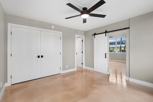 unfurnished bedroom featuring ceiling fan, a barn door, and a closet