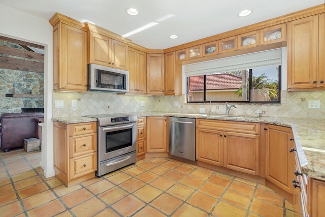 kitchen with sink, backsplash, light stone countertops, and appliances with stainless steel finishes