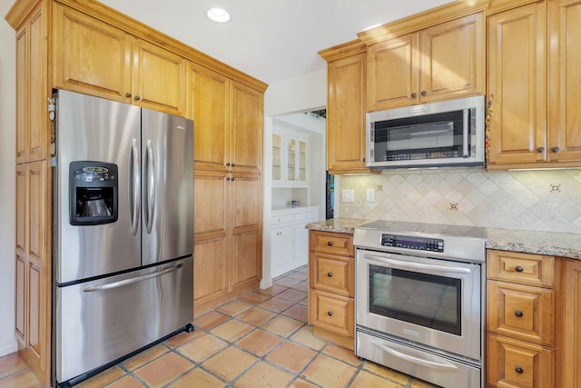 kitchen with appliances with stainless steel finishes, light tile patterned floors, backsplash, and light stone counters