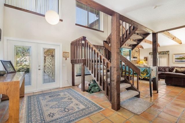 entrance foyer featuring beamed ceiling, a towering ceiling, light tile patterned floors, and french doors