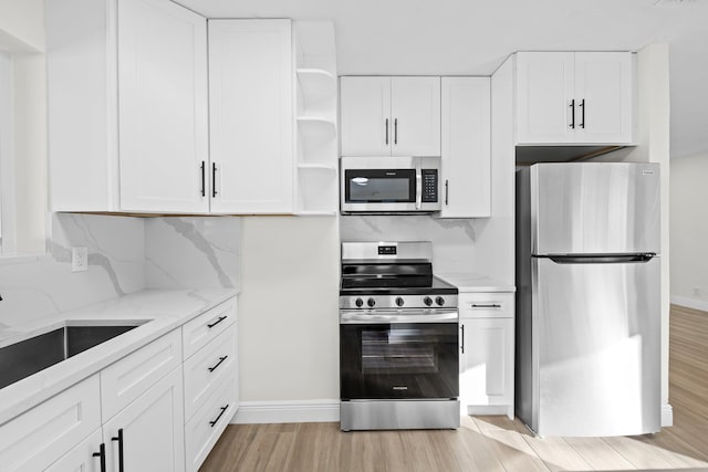 kitchen with light hardwood / wood-style flooring, appliances with stainless steel finishes, light stone countertops, decorative backsplash, and white cabinets