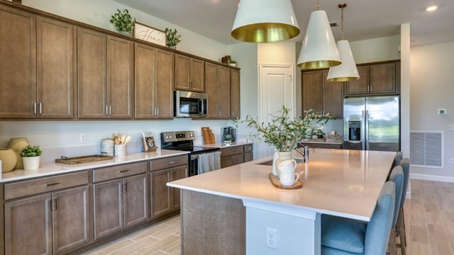 kitchen with sink, a breakfast bar, appliances with stainless steel finishes, a center island with sink, and decorative light fixtures