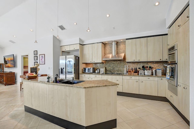 kitchen with wall chimney exhaust hood, sink, pendant lighting, stainless steel appliances, and a kitchen island with sink